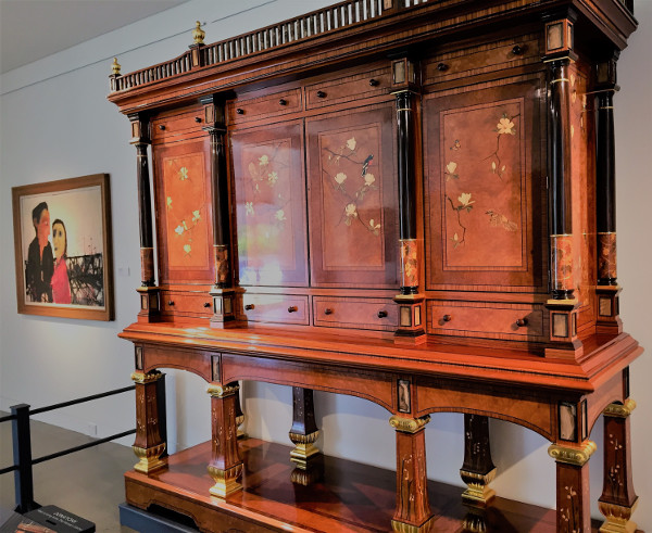 The spectacular Geoff Hannah cabinet is made from 34 different timbers, 4 species of shells and 17 varieties of precious stones. It has marquetry inlays on 18 doors, and features 140 drawers. In the background is Kevin Connor’s ‘Summer Morning, 1963’.